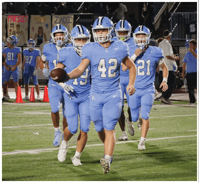 A group of football players wearing blue uniforms are running on the field. AI generated content