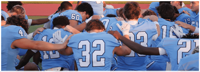 A group of football players in blue uniforms are huddled together on the field. AI generated content