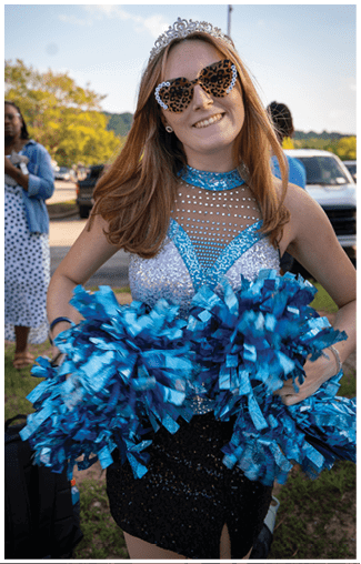 A woman in a blue dress and sunglasses is holding a blue and white pom pom. AI generated content
