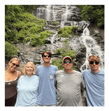 A group of five people, including a man and a woman, pose for a picture in front of a waterfall. AI generated content