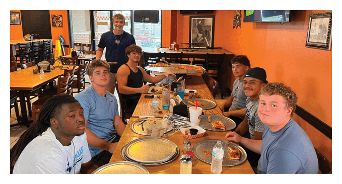 A group of young men are sitting around a table in a restaurant, enjoying pizza and drinks. AI generated content