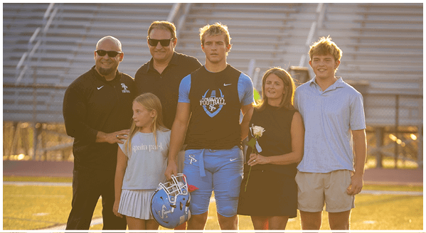 A group of people, including a young man in a football uniform, pose for a photo on a field. AI generated content