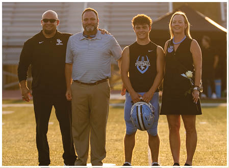 A group of people, including a man and a boy, are standing on a field. The man is wearing a suit and tie, and the boy is holding a football. AI generated content