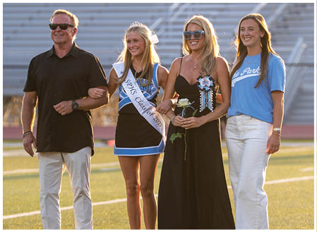 A group of people, including a man and three women, are standing on a field. The women are wearing sashes, and one of them is holding a bouquet of flowers. AI generated content