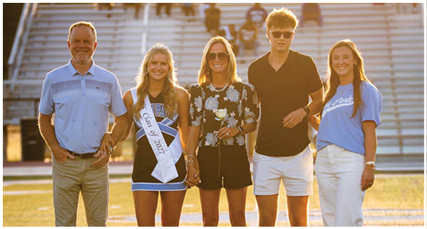 A group of people, including a woman in a blue dress, pose for a photo on a football field. AI generated content