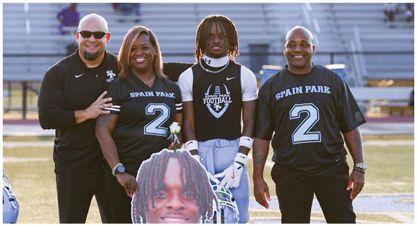 Four people pose for a picture on a field, two of them holding a cutout of a man's face. AI generated content