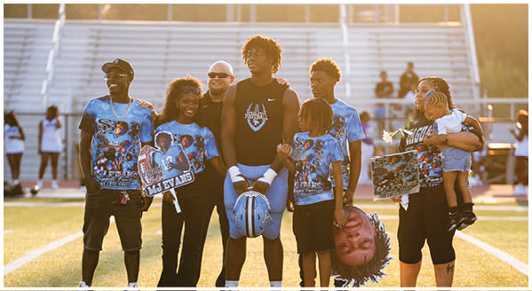 A group of people are standing on a football field, posing for a picture. They are holding up signs and a football jersey. AI generated content