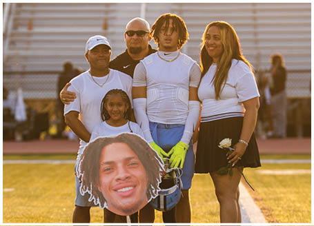 A group of people posing for a photo on a field, with a man holding a football player's head on a cutout. AI generated content