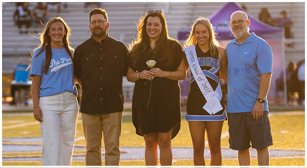 Four people pose for a photo on a football field. A man and woman are holding a trophy, while two other people stand beside them. AI generated content