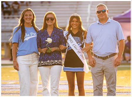 A group of people, including a man and two women, are standing on a field. The man is wearing a blue shirt and sunglasses, while the women are wearing blue and white shirts. One of the women is holding a rose. AI generated content