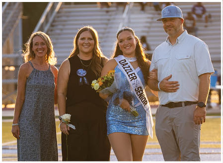 A group of people, including a man, woman, and two girls, are standing on a football field. The woman is holding a bouquet of flowers. AI generated content
