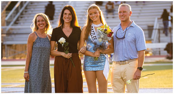 A group of people, including a man and two women, are standing on a field holding flowers. AI generated content