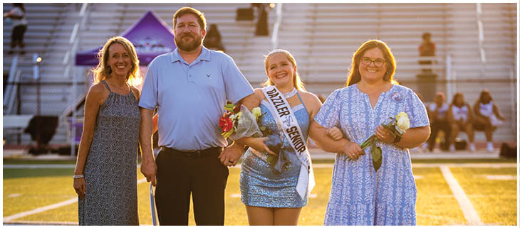 A group of people, including a man and two women, are standing on a field. The man is holding a bouquet of flowers, and the women are holding flowers as well. They are posing for a picture. AI generated content