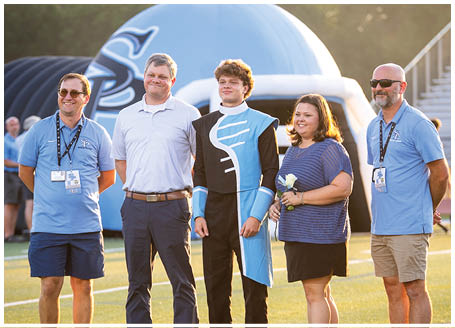Four people are standing on a field, posing for a picture. A man in a suit is holding a rose. AI generated content