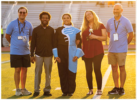 Five people are standing on a field, posing for a picture. They are wearing uniforms and holding flowers. AI generated content