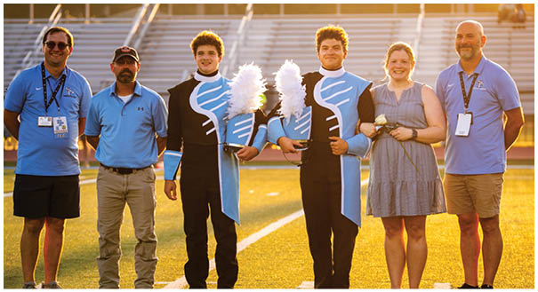 A group of people, including a woman, pose for a picture on a field. They are wearing uniforms and holding instruments. AI generated content