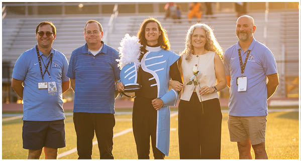 Four people and a woman pose for a photo on a football field. AI generated content