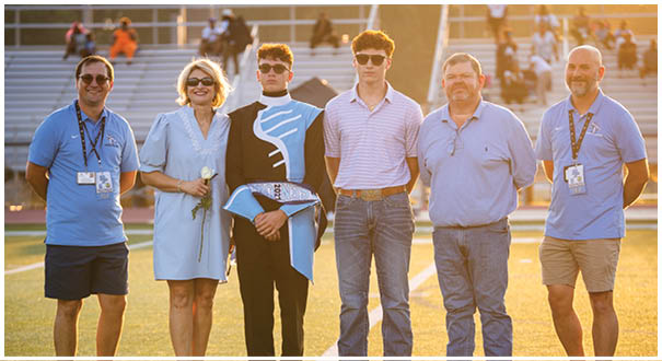 A group of people, including a woman and a man in a band uniform, pose for a photo on a football field. AI generated content