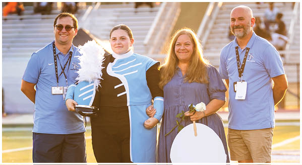Four people are standing on a field, two men and two women. The woman on the right is holding a bouquet of flowers. AI generated content