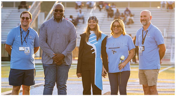 Four people are standing on a field, posing for a picture. They are wearing blue shirts and are accompanied by a woman holding a bouquet. AI generated content