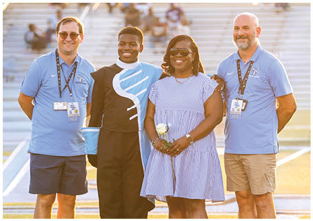 Three people are standing on a field, posing for a picture. One of the individuals is holding a football. AI generated content