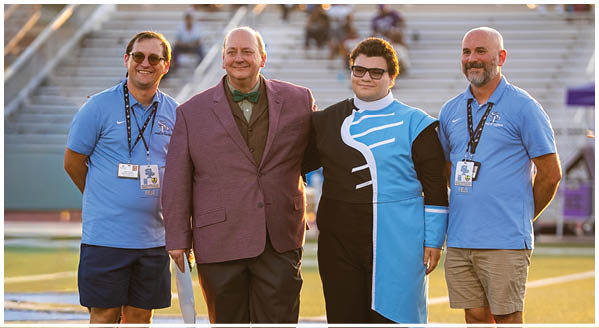 Four people are standing on a field, posing for a picture. Two men are wearing ties, and one of them is wearing a purple jacket. The other two people are wearing blue shirts. AI generated content