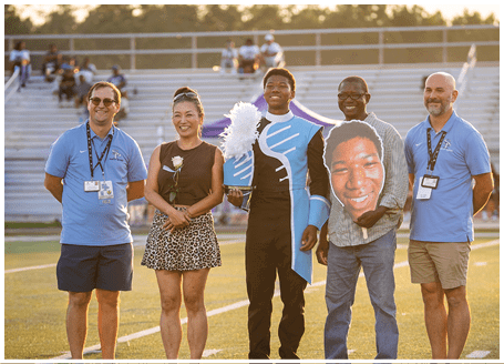A group of people posing for a photo, including a man holding a cutout of another man's face. AI generated content