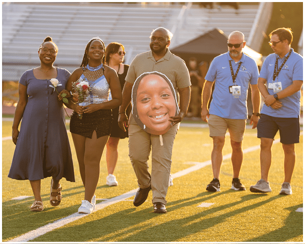 A group of people are walking on a field, one of them is holding a fake head of a smiling woman. AI generated content