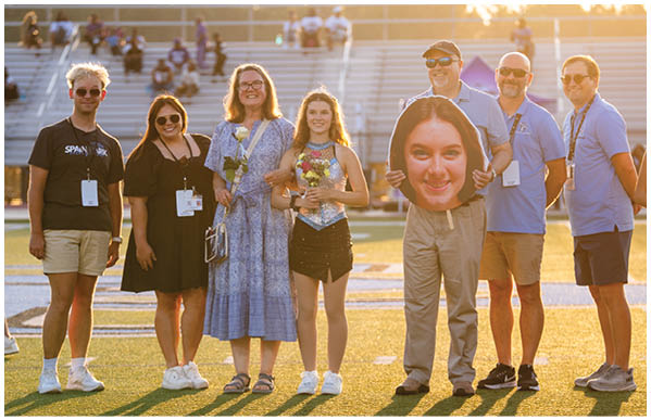 A group of people are standing on a field, posing for a picture. They are wearing name tags and holding flowers. AI generated content