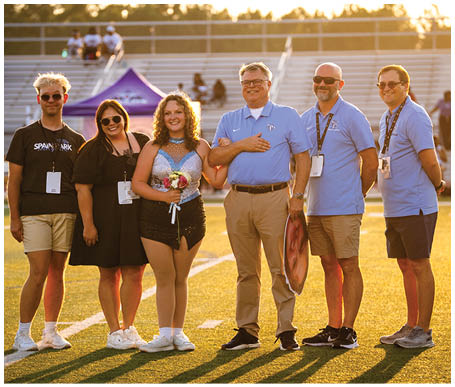 A group of people, including a woman, pose for a photo on a field. AI generated content