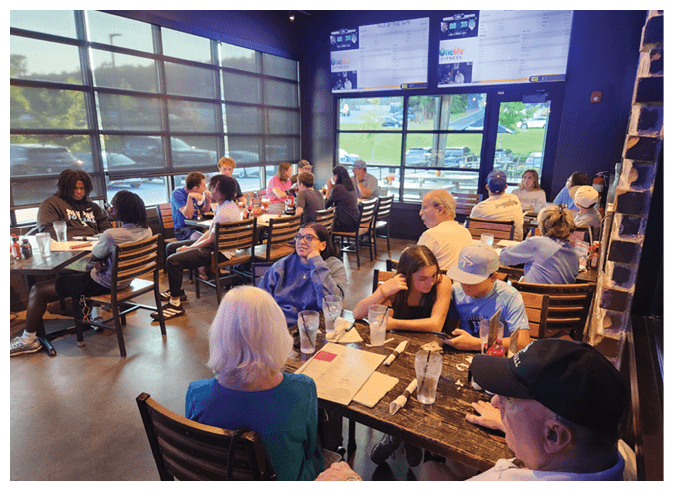 A group of people are sitting at tables in a restaurant, enjoying their meals. AI generated content