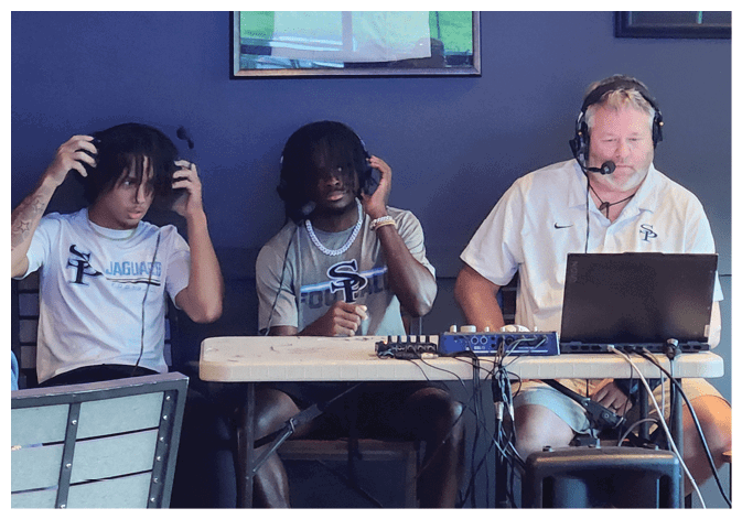 Three men wearing headphones are sitting at a table. One man is wearing a white shirt and another is wearing a black shirt. The third man is wearing a white shirt and a headset. AI generated content
