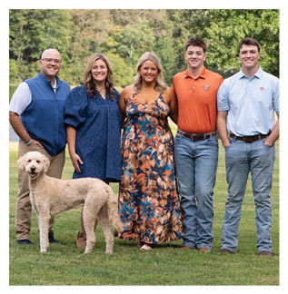 A group of five people and a dog pose for a picture in a grassy field. AI generated content