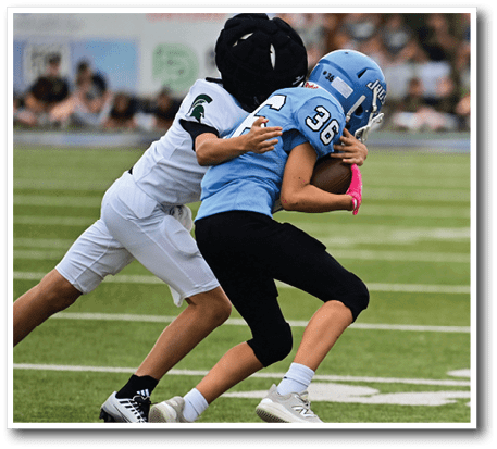 Two football players are on the field, one wearing a blue jersey and the other wearing a white jersey. The blue player is attempting to tackle the white player who is holding a football. AI generated content