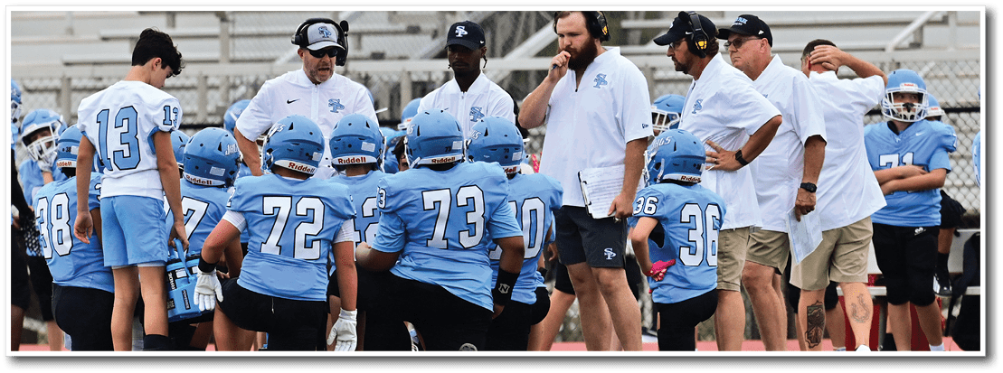 A group of football players in blue uniforms are gathered on the field, engaged in conversation with their coaches. AI generated content