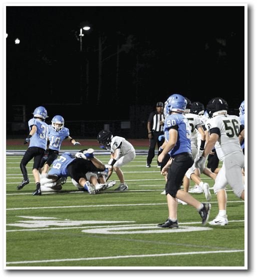 A group of football players on a field, one player is tackled to the ground. AI generated content