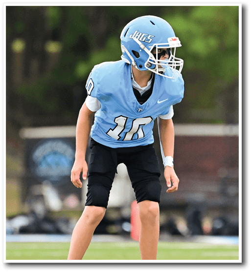 A young boy wearing a football uniform and helmet stands on a field. AI generated content