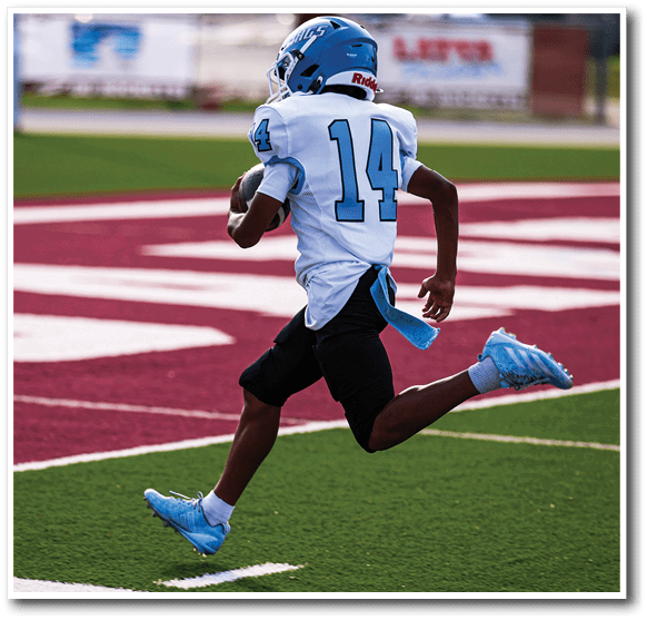 A person wearing a white and blue football uniform with the number 14 is running on a red and white field while holding a football. Description generated by AI