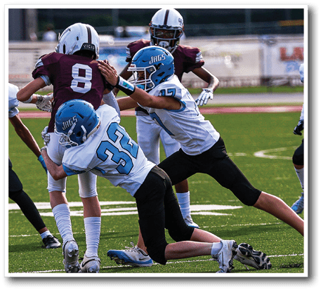 Two people in blue and white football uniforms tackle a person in a maroon and white uniform on a football field during a game. Description generated by AI