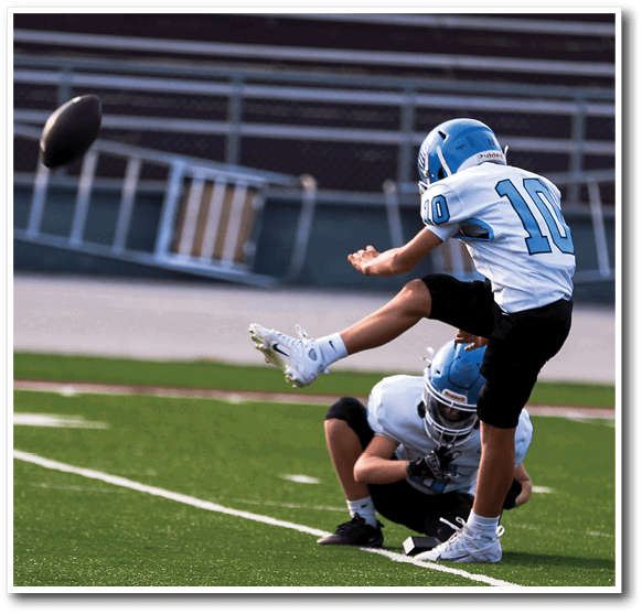 A person wearing a blue helmet and white sports uniform is kicking a football on a field. Description generated by AI