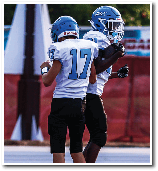 Two people wearing blue helmets and white football jerseys with the number 17 and holding a football are standing on a sports field. Description generated by AI