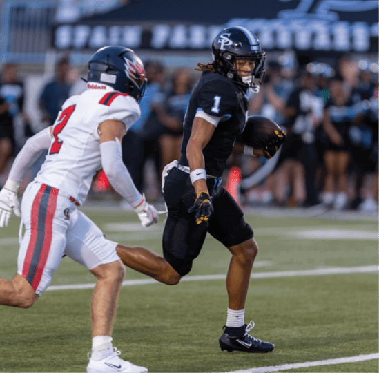 Two people wearing athletic clothing and cleats are running on a football field during a game or practice. Description generated by AI
