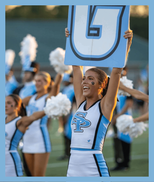 People in cheerleading uniforms are performing with pom-poms and one person is holding up a large sign with the letter G on it. Description generated by AI