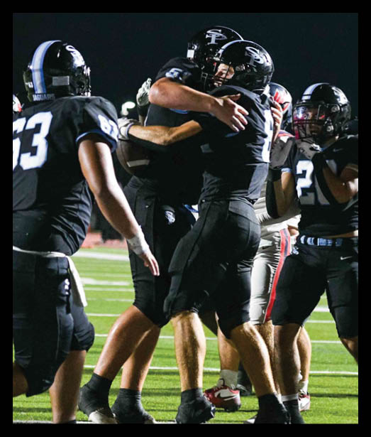 People in black football uniforms are celebrating on a field during a nighttime game. Description generated by AI