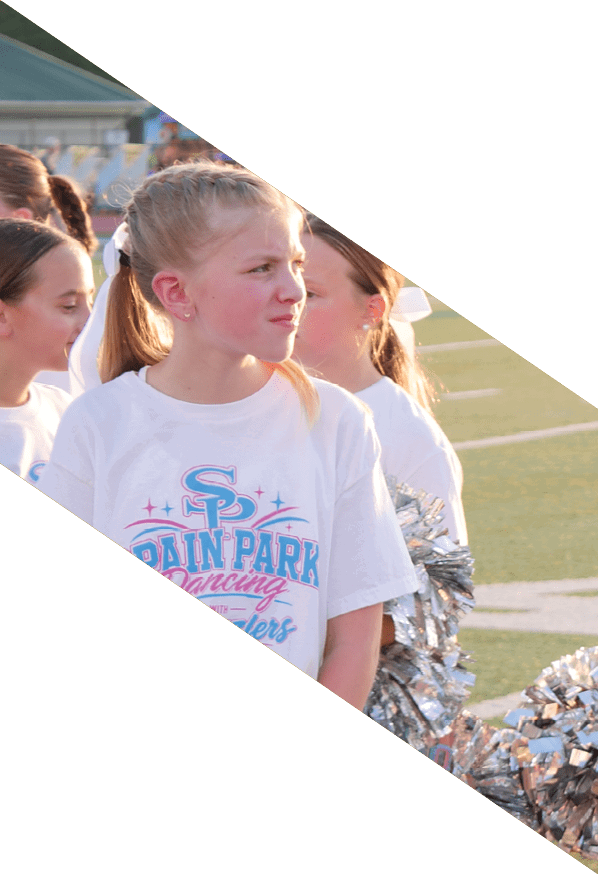 A person wearing a sparkly blue dress is standing on a sports field with bleachers and other people in the background. Description generated by AI