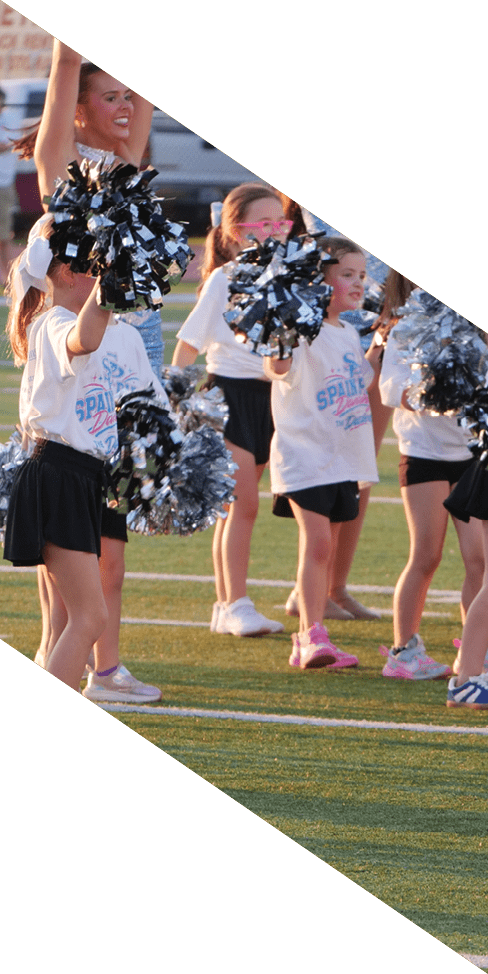 Children in cheerleading uniforms perform a routine on a sports field holding pom-poms. Description generated by AI