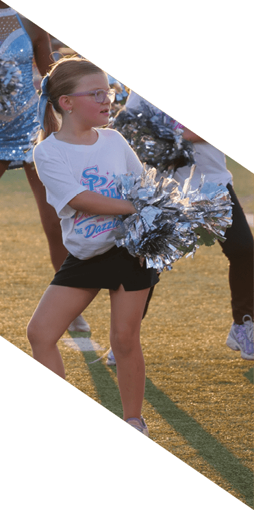 People wearing matching T-shirts and holding silver pom-poms are standing on a grassy field, likely participating in a cheerleading or sports event. Description generated by AI