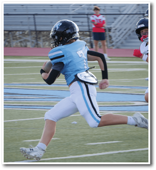 A person in a blue and white football uniform is running with the ball on a field while being chased by a person in a white and red uniform. Description generated by AI