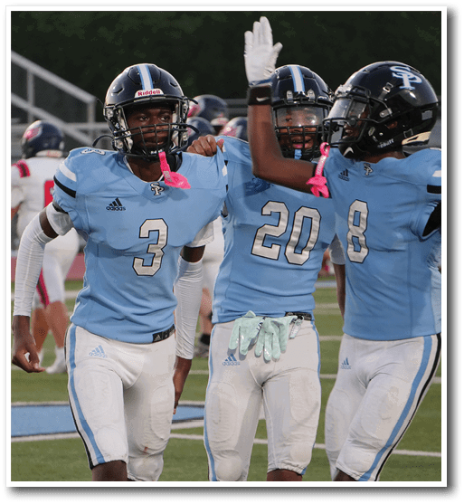 Three people in light blue football uniforms celebrating on a field while two others in white and red uniforms walk away in the background. Description generated by AI