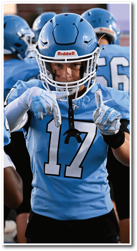 A person wearing a blue football uniform with the number 17 is pointing forward while surrounded by teammates in similar uniforms. Description generated by AI